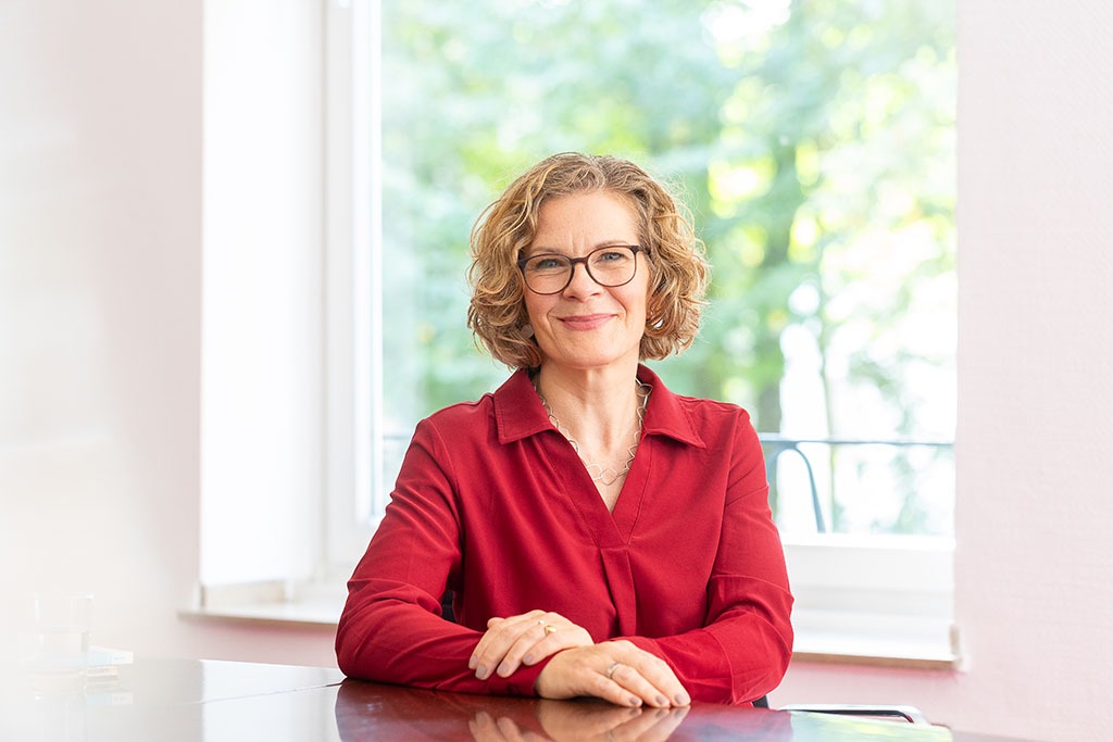 Frau sitzt am Schreibtisch - klassisch porträtiert.