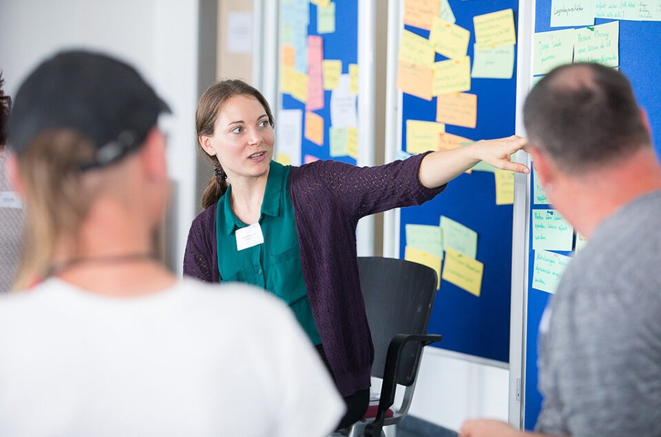 Fotos bei der Kölner Tafel. Eine Person erklärt an einem Flipchart