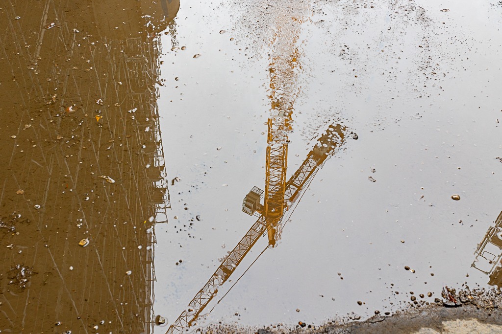 Ein Kran spiegeltsich in einer Pfütze